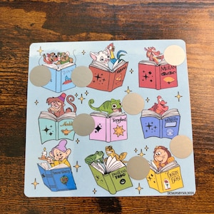 Puede incluir: Una tarjeta azul claro con ilustraciones de personajes de Disney leyendo libros. Los personajes incluyen a Moana, Mulan, Aladdin, Rapunzel, Ariel, Blancanieves, Tiana y Bella. La tarjeta tiene c&iacute;rculos dorados para rascar y el texto "DESIGNSBYSOL2024".