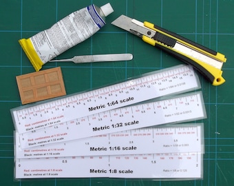 May include: Assortment of model-making tools on a green cutting mat. Includes a tube of glue, a utility knife, a scalpel, a small wooden panel, and several metric scale rulers with ratios from 1:8 to 1:64.