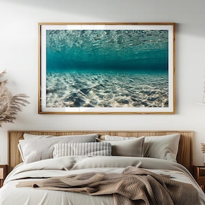 Puede incluir: Una impresión enmarcada de una escena submarina. La imagen captura el juego de la luz en el fondo del océano, con agua ondulante arriba. La paleta de colores está dominada por tonos de azul y blanco, creando un efecto sereno y calmante.