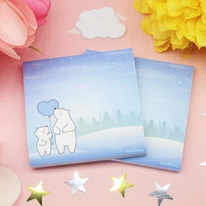 May include: Two polar bears, one holding a blue heart-shaped balloon, stand in a snowy landscape. The image is on a set of two blue and white notepads with a snowy winter scene.
