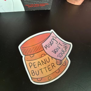 May include: A sticker of a peanut butter jar with a pink note attached that says "Misery's Don't Touch!"