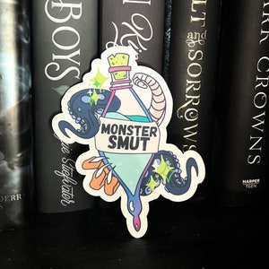 May include: A sticker of a blue bottle with a label that says "Monster Smut". The bottle is surrounded by an octopus and a tentacle. The sticker is on a bookshelf with other books.