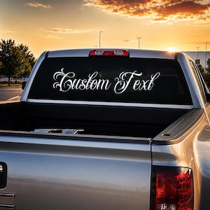 May include: A silver pickup truck with a white vinyl decal applied to the rear window. The decal features the words Custom Text written in a decorative, flowing script font with elegant flourishes on the capital C and T characters.