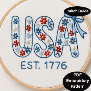 May include: Embroidered hoop art featuring the word "USA" in blue, red, and white floral designs. The text "EST. 1776" is below the word. The design is set in a wooden embroidery hoop. Includes "Stitch Guide" and "PDF Embroidery Pattern" text.