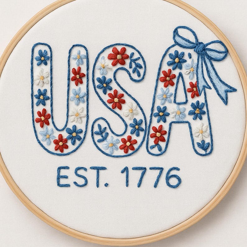 K&ouml;nnte beinhalten: Gesticktes Wandbild mit dem Wort "USA" in Blau, gef&uuml;llt mit roten, wei&szlig;en und blauen Blumenmustern. Der Text "EST. 1776" ist darunter gestickt. Das Design befindet sich in einem Holzreifen.