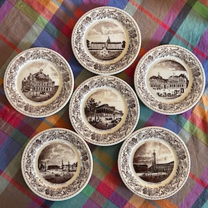 May include: A set of five round ceramic plates featuring brown transferware illustrations of Paris monuments. Each plate has a detailed floral border and a central scene depicting landmarks like the Opera, Les Invalides, and Place Vendome.