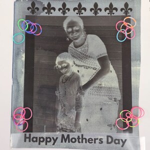 May include: A black and white photo of a mother and child. The photo is in a frame with a fleur-de-lis design. The photo is surrounded by colorful rubber bands. The text "Happy Mothers Day" is printed below the photo.