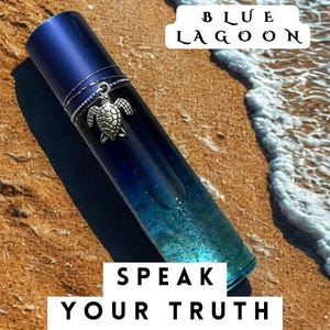 May include: A cylindrical glass bottle with a dark blue to light blue gradient finish containing liquid with glitter. A silver-toned sea turtle charm hangs from a thin chain wrapped around the neck. Text reads BLUE LAGOON and SPEAK YOUR TRUTH.