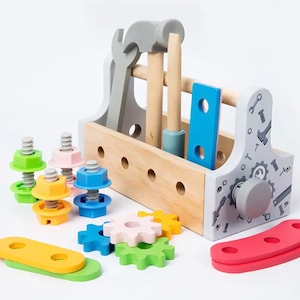 May include: A wooden toy toolbox with a gray hammer, wrench, and screwdriver. The toolbox has a blue and pink handle and comes with colorful gears, nuts, and bolts.