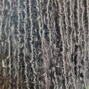 May include: Close-up of dark gray faux locs with a wavy texture. The locs are tightly coiled and have a natural, textured appearance. The image showcases the intricate details of the hair extensions.