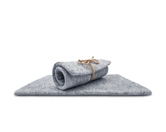 May include: A rectangular light grey felt mat with a textured, mottled surface. A portion of the mat is rolled up and secured in the centre with a thin, natural-coloured jute twine tied in a simple bow, creating a layered and compact appearance.