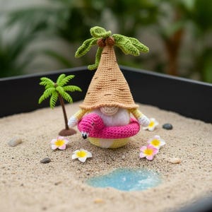 以下が含まれることがあります： 麦わら帽子とピンクのフラミンゴ浮き輪をつけたかぎ針編みのノーム。小さなヤシの木と花のある砂浜のシーンに配置されています。ノームは、緑の葉と黄色の体を持つ、ベージュの円錐形の帽子をかぶっています。