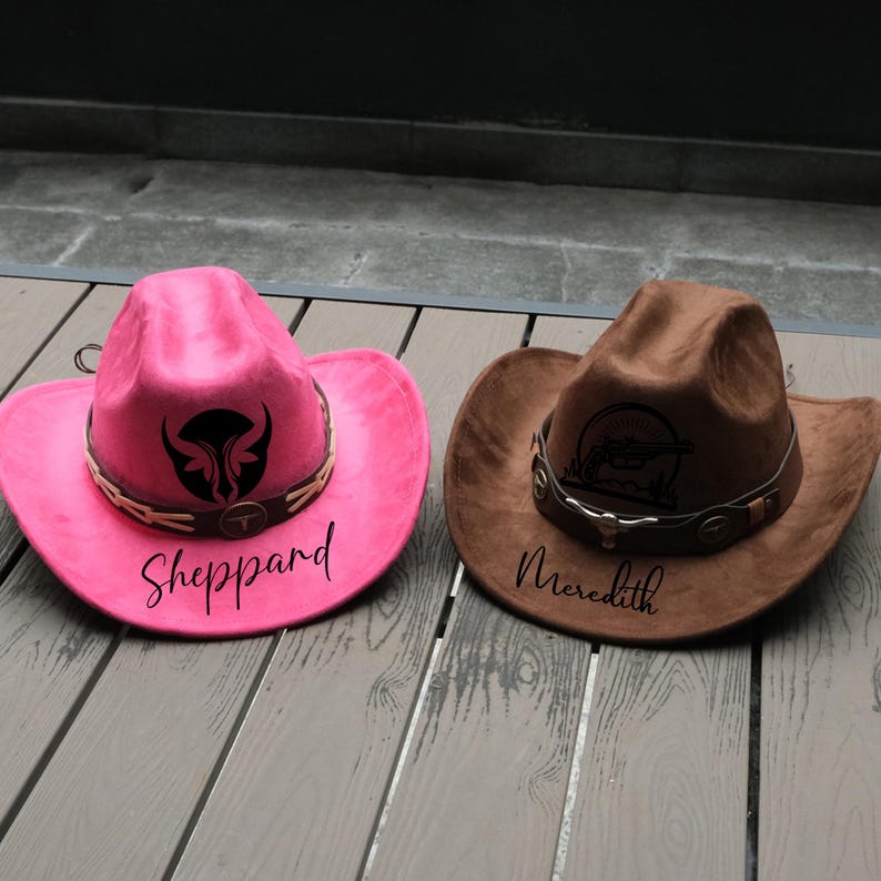 May include: Two cowboy hats. One is bright pink with a black graphic and the name "Sheppard" in black script. The other is brown with a graphic and the name "Meredith" in black script. Both have a decorative band.