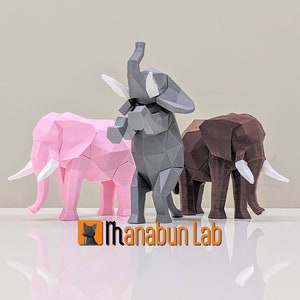 Könnte beinhalten: Drei 3D-gedruckte Elefantenfiguren, eine graue, eine rosa und eine braune, die auf einer weißen Oberfläche stehen. Die Elefanten sind stilisiert und haben ein geometrisches Design.