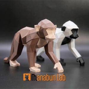 May include: Two geometric monkey sculptures. One is brown and tan, the other is white and black. The sculptures are in a walking pose, with the brown monkey in front. The logo "Ihanabun Lab" is in the bottom corner.