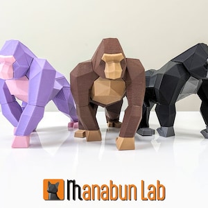 Könnte beinhalten: Drei Low-Poly-Gorilla-Figuren in verschiedenen Farben: Lila, Braun und Schwarz. Die Figuren stehen auf einer weißen Oberfläche.