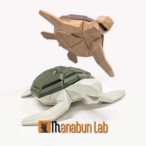 Op de afbeelding: Twee geometrische origami-schildpad-sculpturen. Eén schildpad is bruin en de andere is wit met een groene schild.