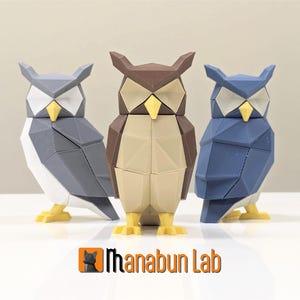 Könnte beinhalten: Drei geometrische Eulenfiguren, eine graue, eine braune und eine blaue. Die Eulen sind aus einem 3D-gedruckten Material gefertigt und haben ein polygonales Design.