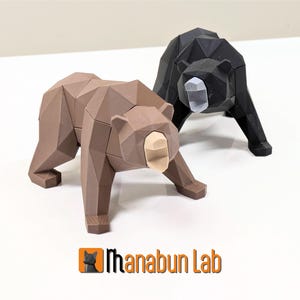 May include: Two geometric bear sculptures, one brown and one black, with a low-poly design. The bears are facing forward with their mouths open, showing their teeth. The sculptures are made of a smooth, matte material.