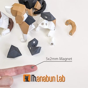 May include: A collection of geometric paper dog models in various stages of assembly, featuring brown, black, and white sections. A 5x2mm magnet is shown, along with the "Manabun Lab" logo.