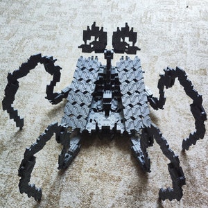 May include: A gray, articulated, plastic toy robot with multiple legs and arms. The robot is posed in a standing position with its legs and arms extended.