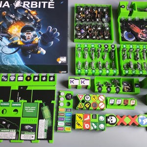 May include: A board game titled "NA ORBITE" with a space theme. The game includes a box, green plastic game pieces, cards, and miniature figures. The box art features an astronaut in space. The game pieces are arranged on a gray surface.