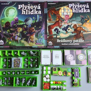 May include: Two board game boxes with the title "Plyšová hlídka" and "Bráškovy patálie" are displayed, along with various game components. The boxes feature colorful illustrations of cartoon characters. Green plastic trays hold game pieces, cards, and dice.