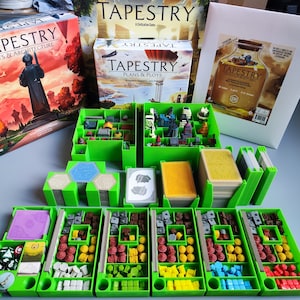 Puede incluir: Cajas de almacenamiento verdes para el juego de mesa Tapestry. Las cajas están llenas de varios componentes, incluyendo piezas de madera, cartas y dados. Las cajas están etiquetadas con los nombres de las diferentes expansiones del juego, incluyendo "Arts & Architecture", "Plans & Ploys" y "The Crossroads of Civilization".