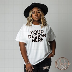 May include: A white t-shirt with the text "YOUR DESIGN HERE" printed in black. The shirt is being modeled by a person wearing a black hat and black jeans.