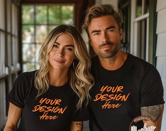 May include: Two people wearing black t-shirts with the text "Your Design Here" printed in orange. The couple is standing in front of a white wooden porch.