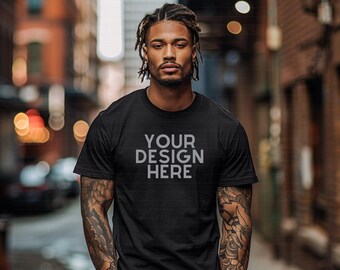 May include: Black crew neck t-shirt with the text "YOUR DESIGN HERE" in a light grey font. The model is wearing blue jeans. The background is a blurred urban scene.