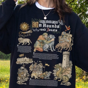 May include: Black sweatshirt with a medieval-themed graphic. The design includes illustrations of dogs, knights, a dragon, and the text "On Hounds and Beasts." The sweatshirt has a white collar and the Gildan Black label.