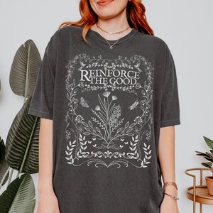 May include: A dark gray oversized t-shirt with a white graphic design featuring a floral border and the text "Reinforce the Good".