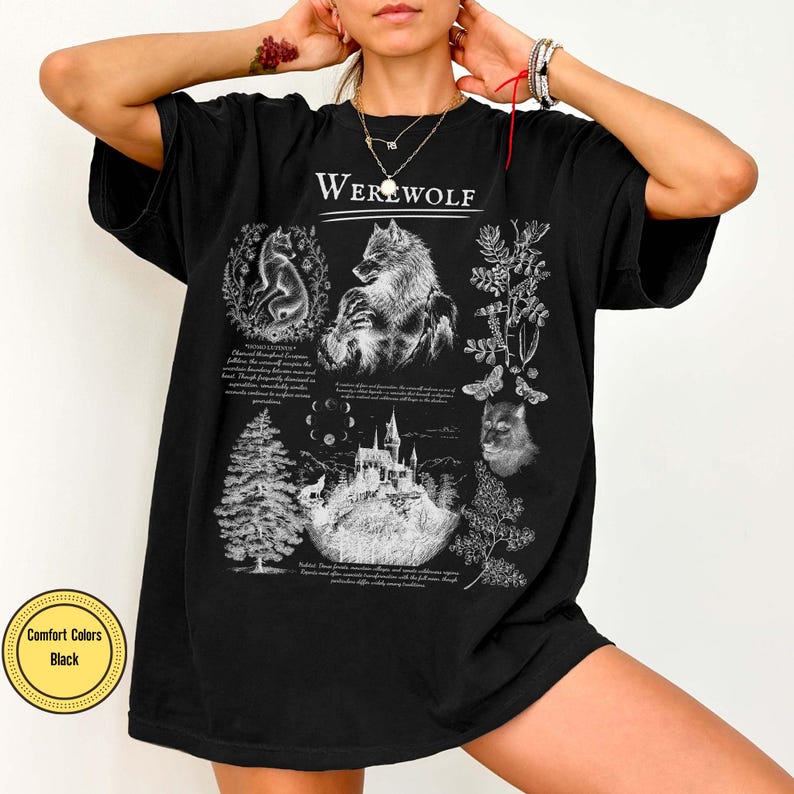 May include: A black short-sleeve t-shirt featuring a white graphic print with the text "WEREWOLF" at the top. The design includes illustrations of a wolf, a castle, a pine tree, moon phases, and botanical elements with small text blocks.