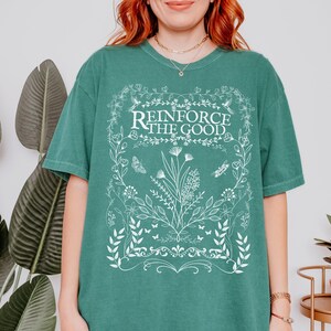 May include: A teal green t-shirt with a white floral design and the text "Reinforce the Good".