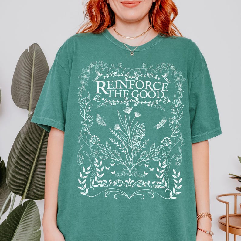 May include: A teal green t-shirt with a white floral design and the text "Reinforce the Good".