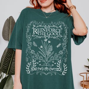 May include: A dark green t-shirt with a white floral design and the text "Reinforce the Good".