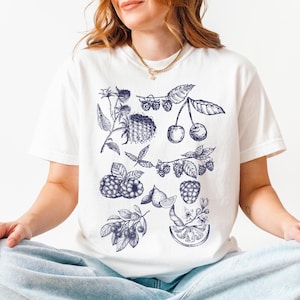 May include: White t-shirt with a blue and white illustration of various fruits and berries, including cherries, raspberries, and blueberries.