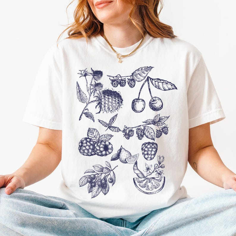 May include: White t-shirt with a blue and white illustration of various fruits and berries, including cherries, raspberries, and blueberries.