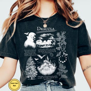 Op de afbeelding: Zwart Comfort Colors T-shirt met een grafisch ontwerp met het woord "Dracula". Het ontwerp bevat illustraties van een kasteel, vleermuizen, een koets en tekst. Het shirt heeft een vintage uitstraling.