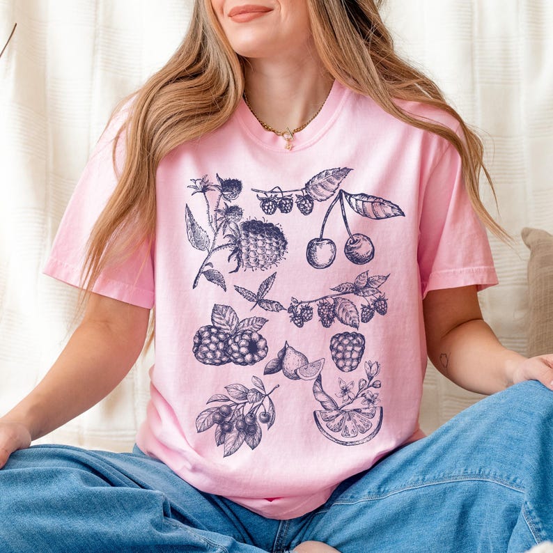 May include: A pink t-shirt with a blue and white graphic print of various fruits and berries, including cherries, raspberries, and blueberries.
