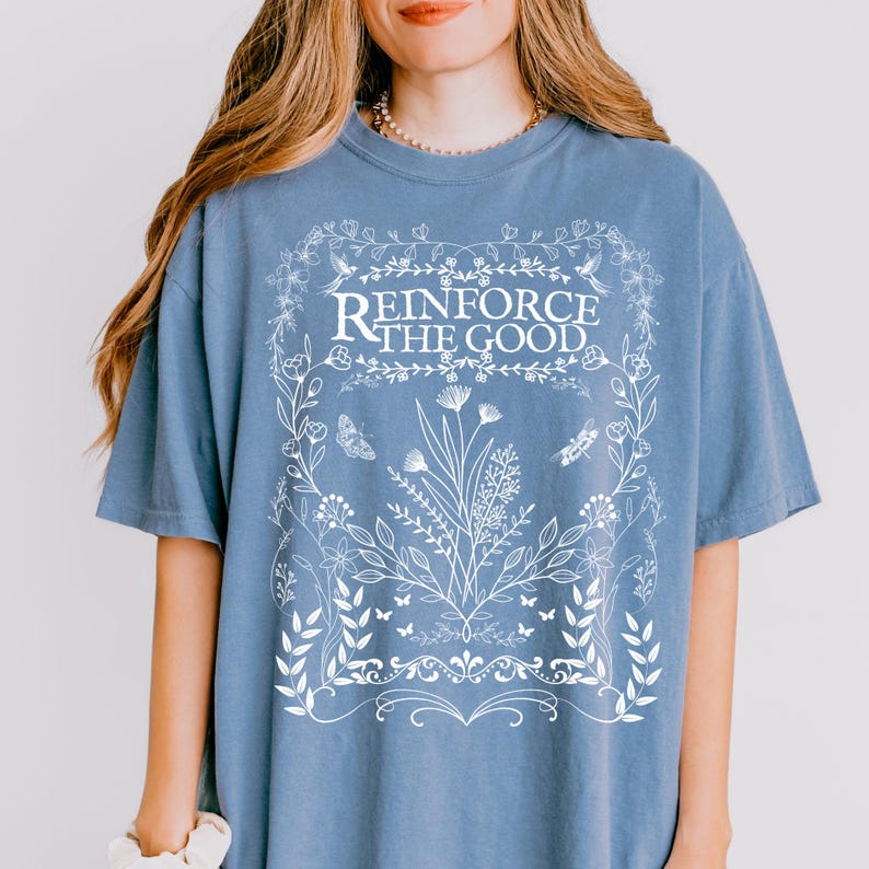 May include: A light blue t-shirt with a white floral design and the text "Reinforce the Good" in a white banner.