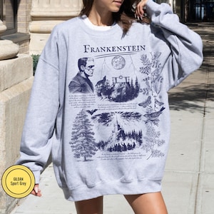 May include: Sport grey sweatshirt with a graphic design featuring the word "Frankenstein" and illustrations of a monster, a full moon, a forest, and text. The sweatshirt has a crew neck and long sleeves.