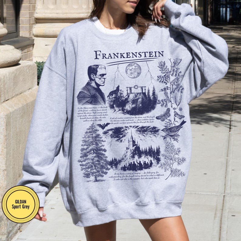 May include: Sport grey sweatshirt with a graphic design featuring the word "Frankenstein" and illustrations of a monster, a full moon, a forest, and text. The sweatshirt has a crew neck and long sleeves.