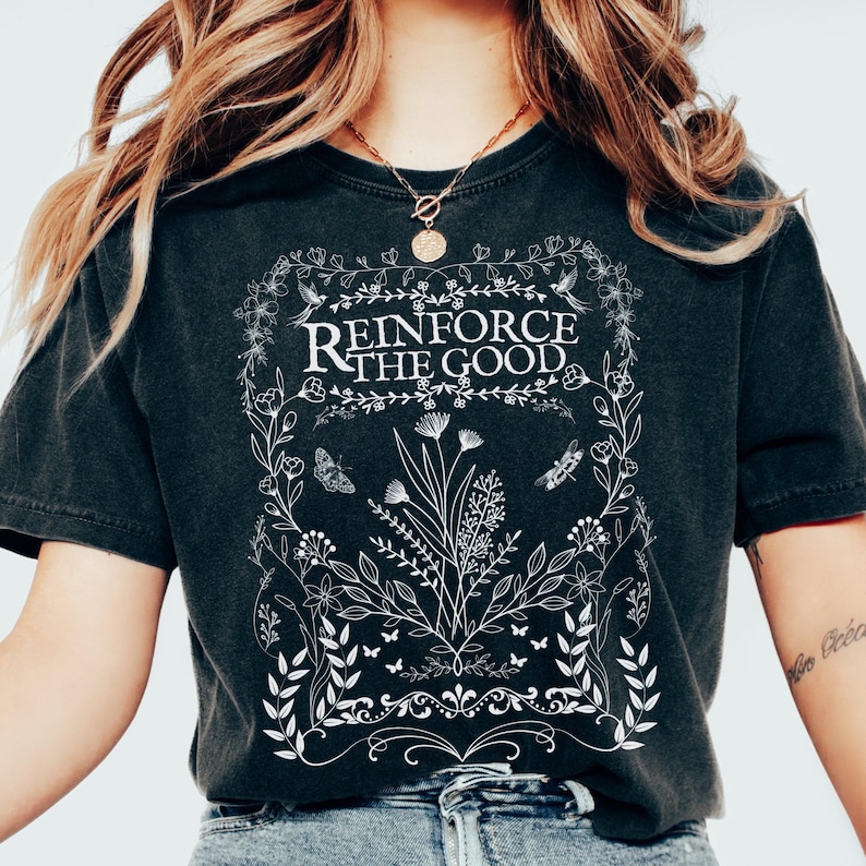 May include: Black t-shirt with a white floral design and the text "Reinforce the Good" in a vintage style font.