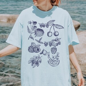 May include: A light blue t-shirt with a vintage style print of various fruits and berries, including cherries, raspberries, and blueberries.