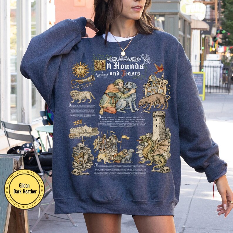 May include: Dark heather blue sweatshirt with a graphic design featuring illustrations of dogs, a dragon, and text that reads "On Hounds and Beasts." The design includes medieval-style drawings and text.