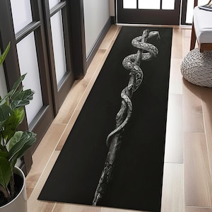 Può includere: Tappeto rettangolare nero con un'immagine in scala di grigi di un serpente avvolto attorno a un ramo d'albero. Il serpente e il ramo sono dettagliati sullo sfondo scuro. Il tappeto è posto in un corridoio. La lunghezza del tappeto è di circa 180 cm.