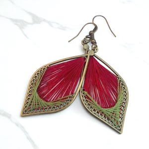 Può includere: Orecchini a forma di foglia con montatura in metallo color bronzo e bordo dettagliato. L'interno è riempito di filo rosso, con dettagli in filo verde. Chiusura a gancio. Gioiello unico.