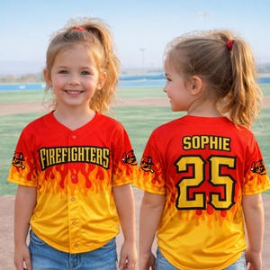May include: A red and yellow baseball jersey with the word "FIREFIGHTERS" in black and yellow lettering. The jersey has a flame design and the number 25 on the back with the name "SOPHIE".